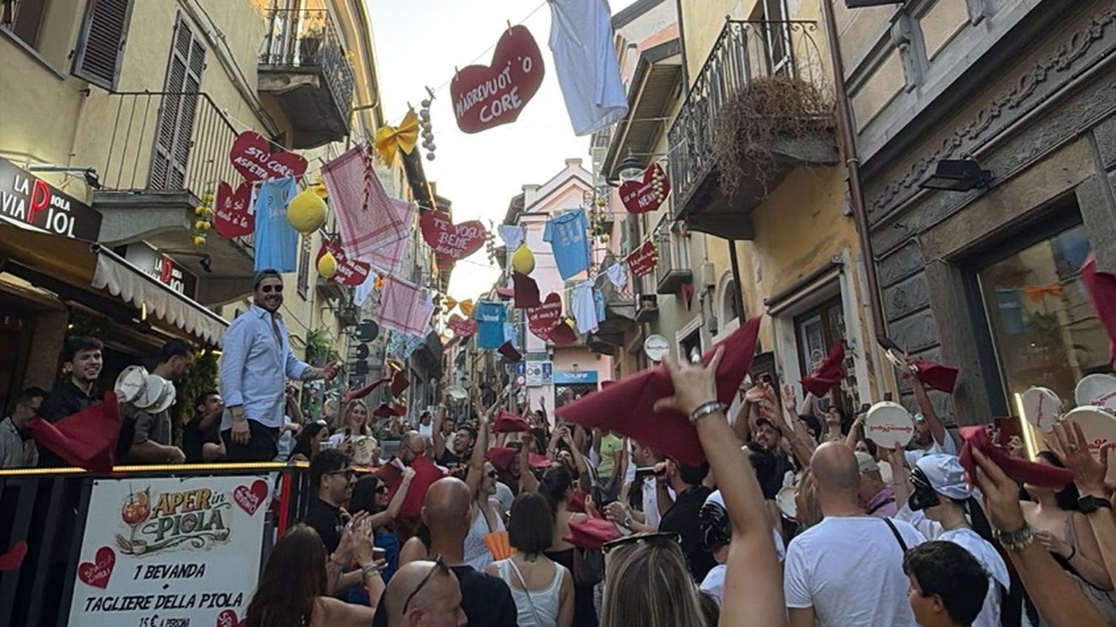 Mani e tamburelli alzati in mezzo alla via addobbata a una festa SpaccaNapoli